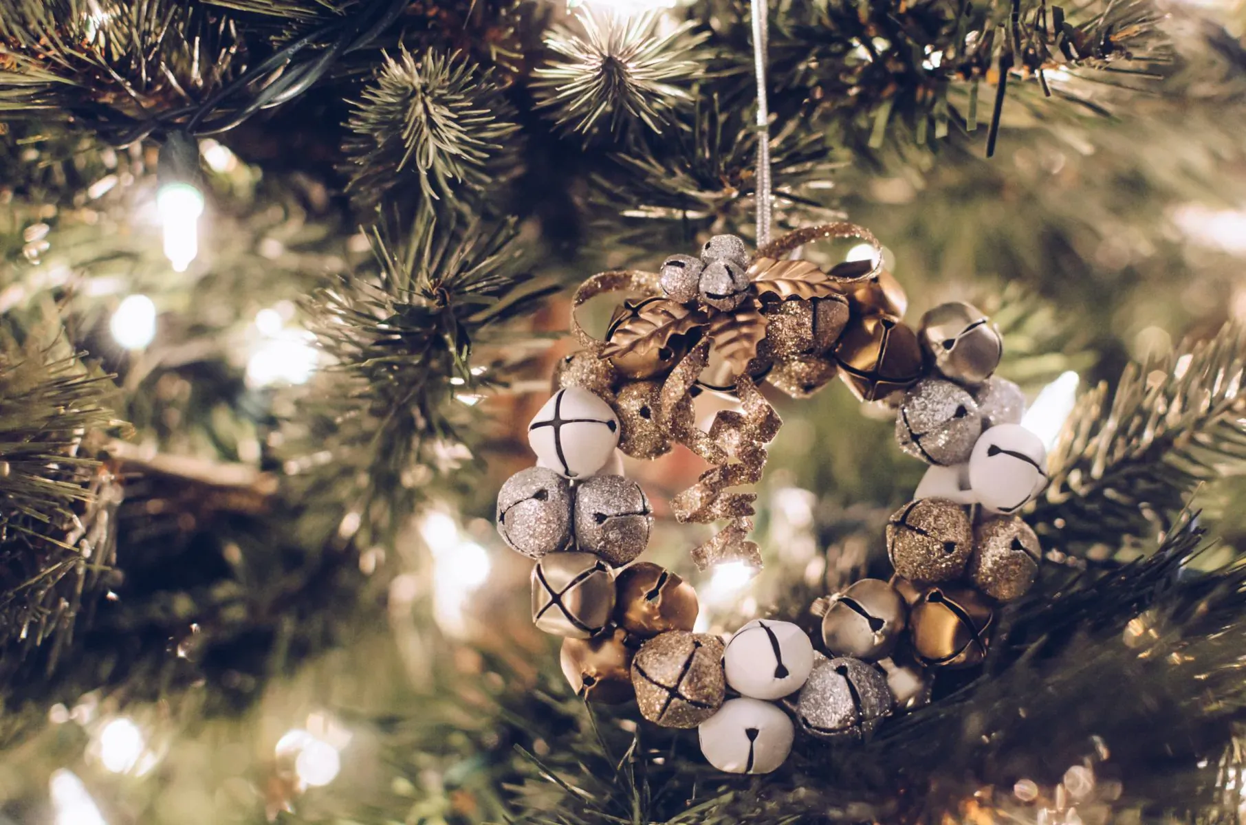 Elegant Christmas wreath of white and gold jingle bells hanging on a lit evergreen tree branch
