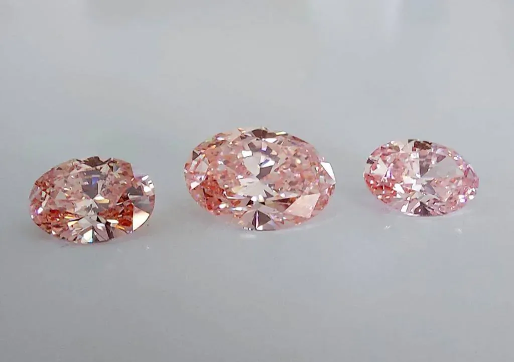 Three pink lab-grown diamonds in round and oval cuts on white background