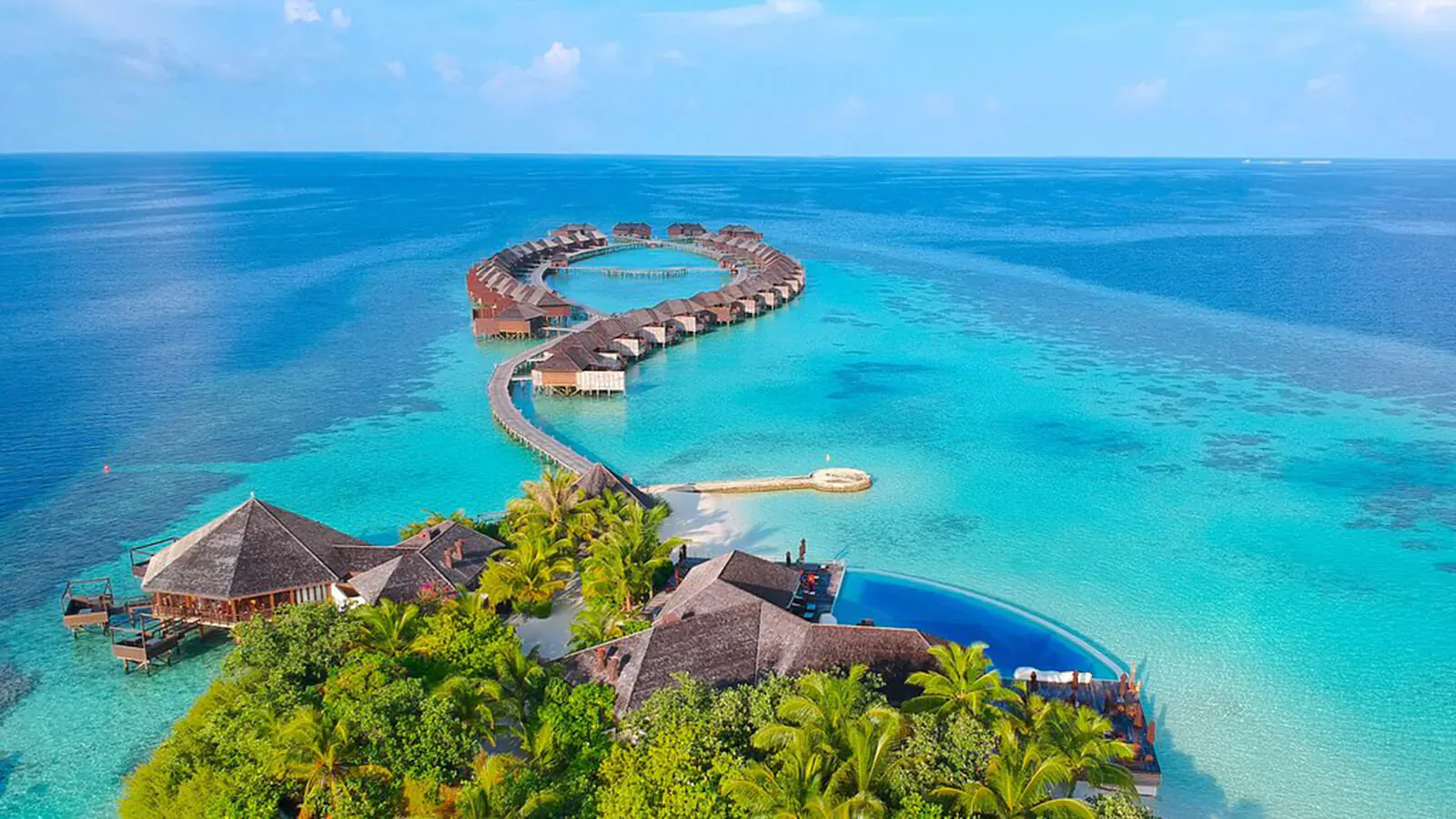 Aerial view of Lily Beach Resort & Spa's overwater bungalows curving over turquoise Maldives lagoon with infinity pool.