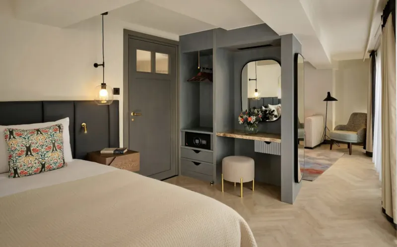 Modern hotel room at The Reach at Piccadilly, Manchester, with king bed, vanity mirror, armchair, and herringbone floors.