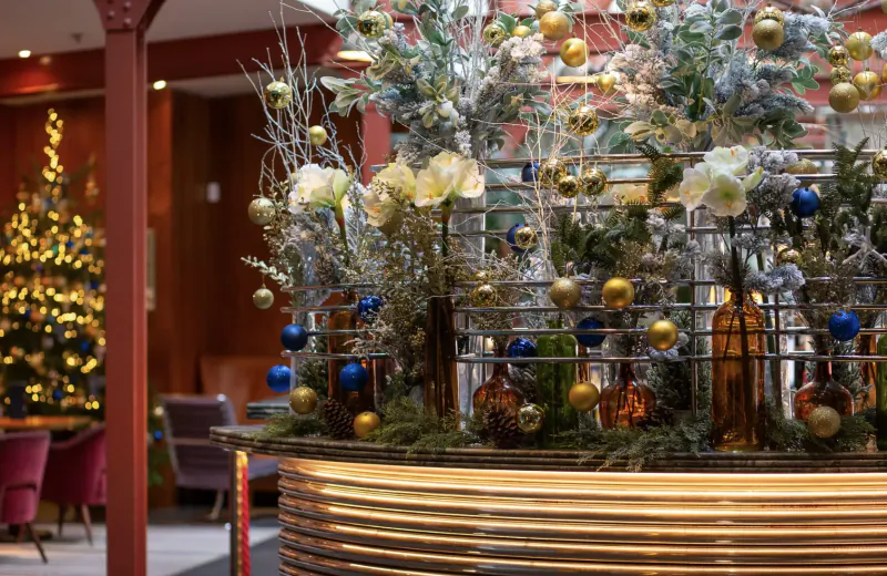 Festive floral Christmas display with gold, blue ornaments and trees in Bluebird Chelsea lobby