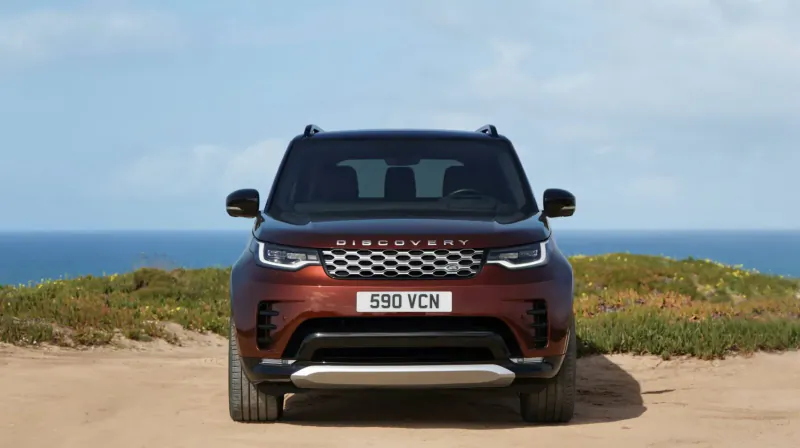 Front view of maroon Land Rover Discovery SUV with license plate 59 FCN on coastal cliff overlooking ocean.