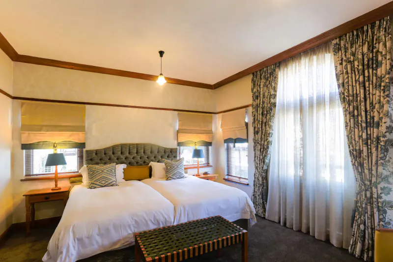 Elegant Eendracht Hotel bedroom with twin white beds, wooden headboard, lamps, curtains, and window.