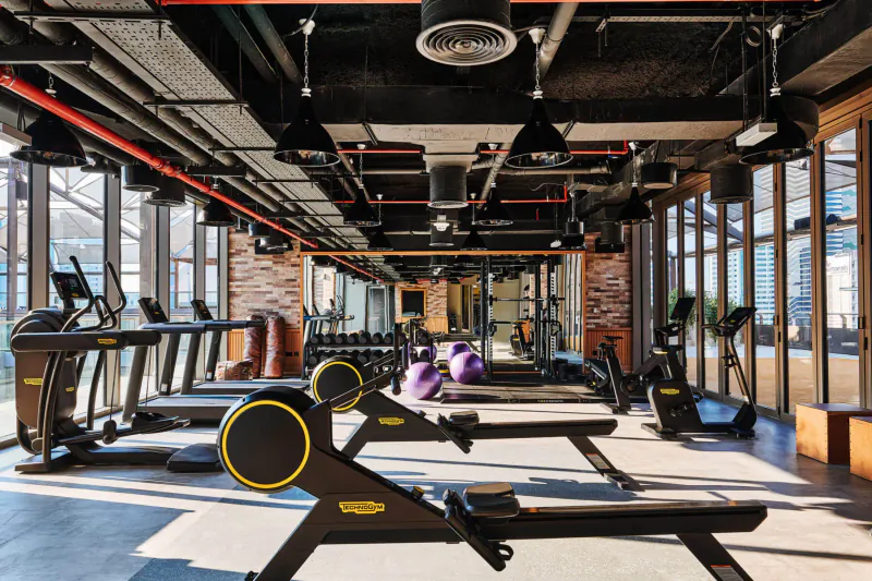 Spacious modern gym at 25hours Hotel One Central Dubai with treadmills, rowers, weights, and large windows.
