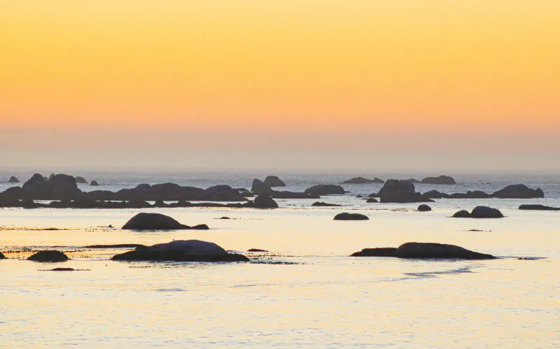 Sunset over calm ocean waves and scattered rocks at Paternoster beach