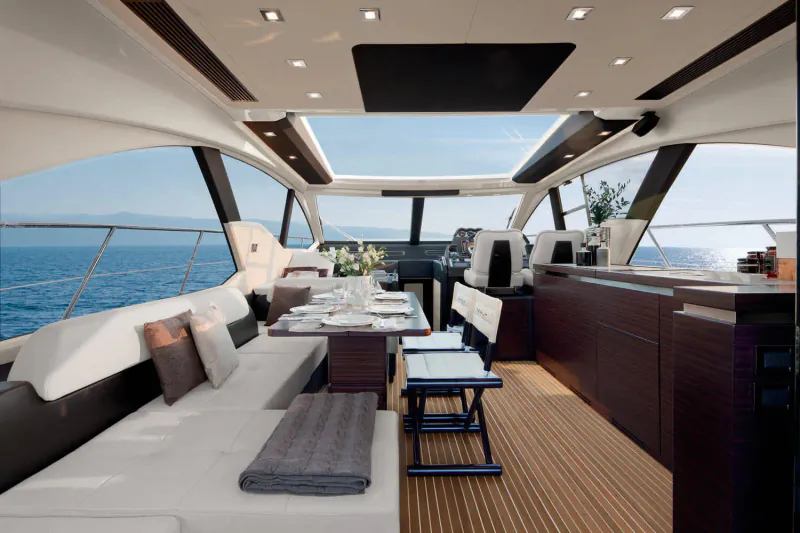 Luxurious modern yacht interior with white leather seating, dining table, wooden floors, and sea view.