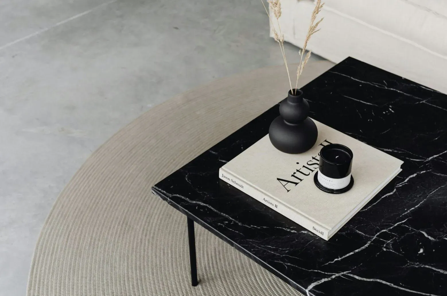 Luxe black marble coffee table with open 'Artist' book, black vase of pampas grass, and white candle on beige rug.