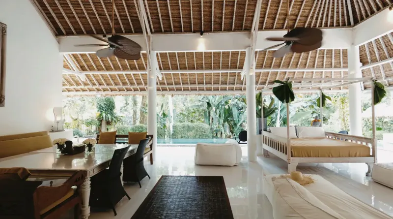 Luxurious open-plan Balinese villa interior with thatched ceiling, dining area, pool, and tropical garden view
