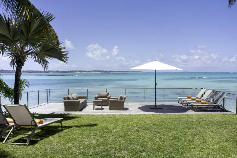 Villa Ruby deck at Villas de Maitre Mauritius, Belle Mare beach: lounge chairs, sofa set, white umbrella, ocean view with palms.