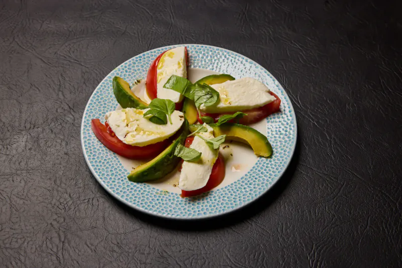 Caprese salad with fresh mozzarella, tomatoes, avocado, and basil on a blue plate