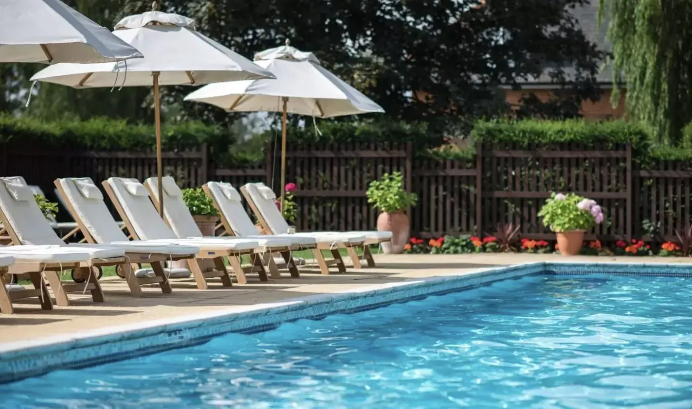 Serene poolside at Champneys Forest Mere with white loungers under umbrellas, potted plants, and trees.