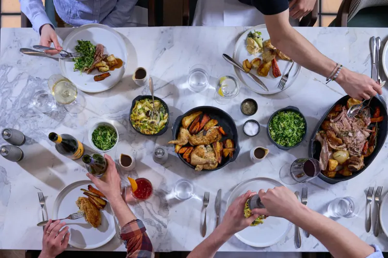 Top-down view of Sunday roast lunch at Treadwell Restaurant: roast beef, chicken, roast potatoes, greens, wine on marble table.