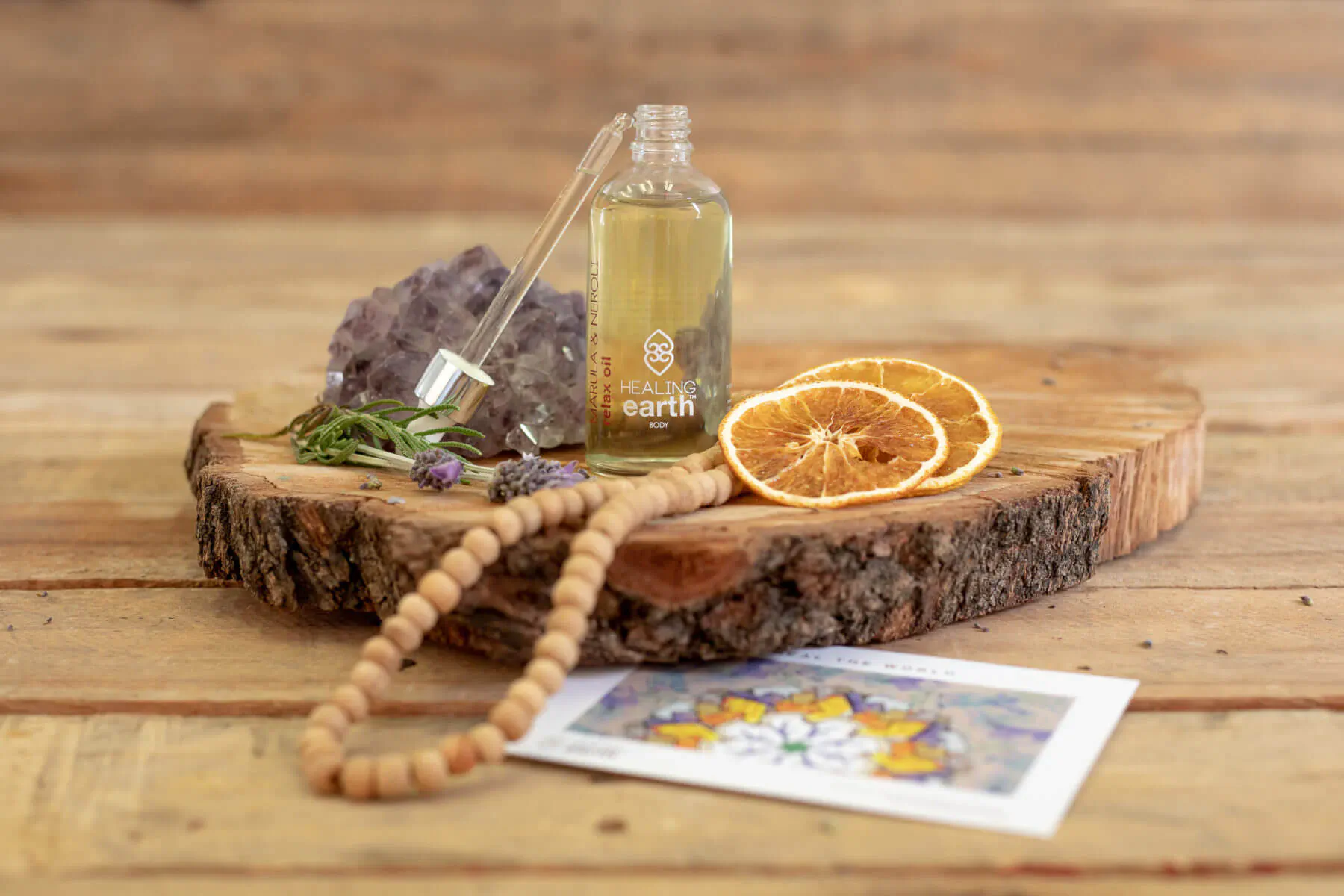Dropper bottle of golden oil on wooden slice with amethyst, orange slices, wooden beads, rosemary, and wellness card