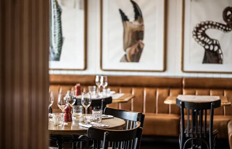 Cozy restaurant interior with leather booths, round table set with wine glasses, condiments, and abstract crab art on walls at Battersea Power Station.