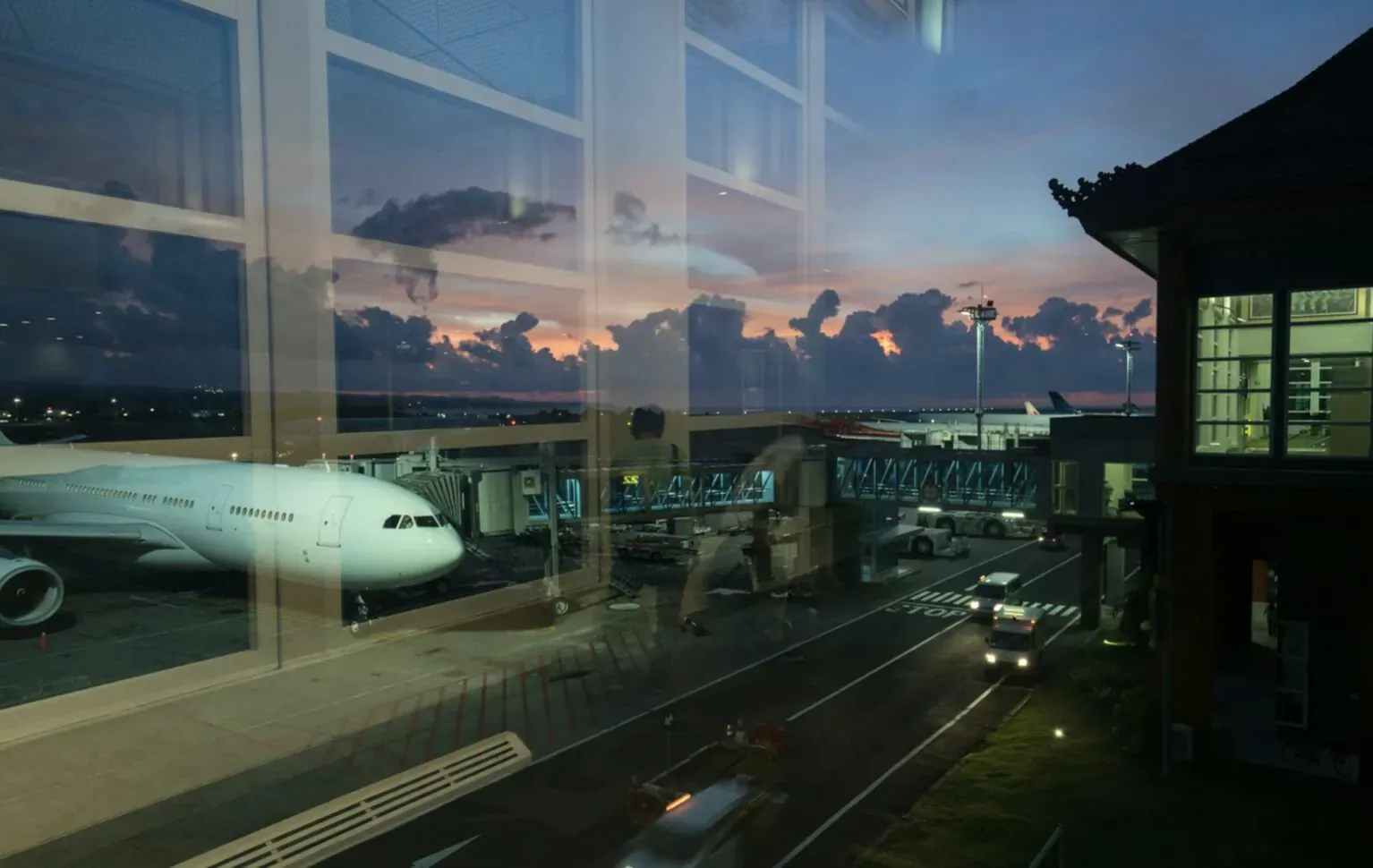 White airliner at jet bridge in airport terminal, sunset sky through glass windows, adjacent pagoda-style building