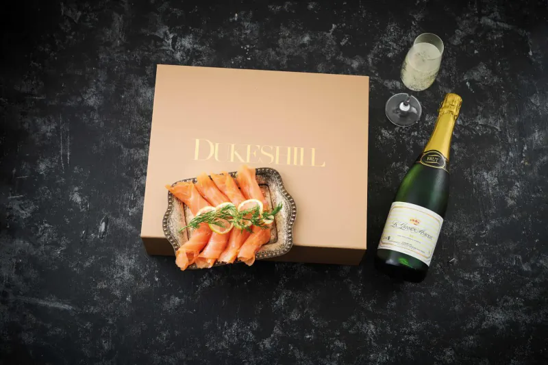Dukeshill box with smoked salmon on black slate, champagne bottle, and flute on dark surface