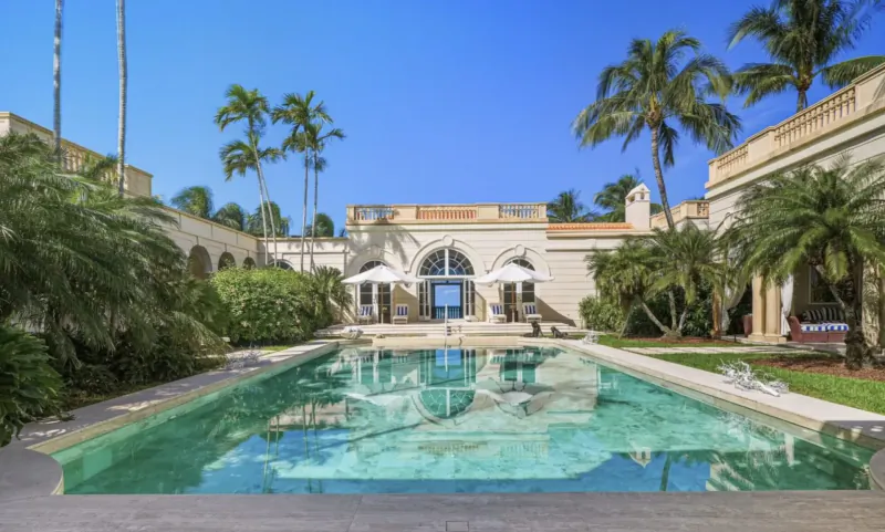 Luxurious Sans Souci estate in Lyford Cay, Bahamas: Mediterranean-style villa with pool, palms, and umbrellas under blue sky.