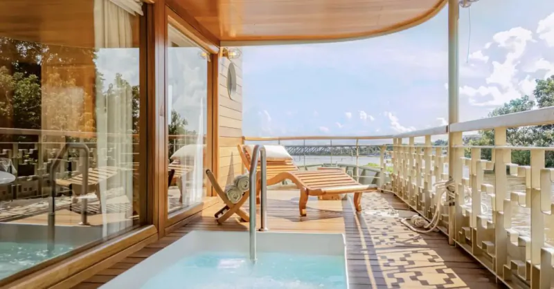 Luxurious wooden villa balcony with bubbling hot tub, lounge chairs, and scenic lake view.