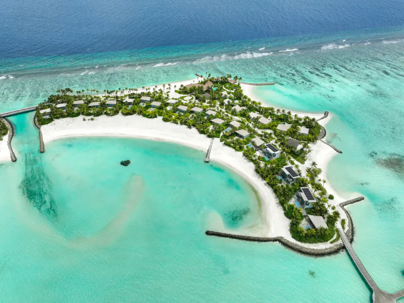 Aerial view of Crossroads Maldives resort on lush tropical island with white sand beach and turquoise lagoon