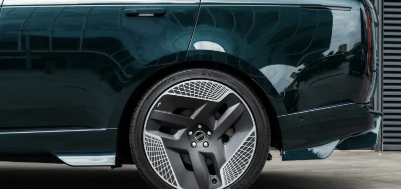 Rear side view of Racing Green luxury SUV with striking black multi-spoke wheels against garage door.