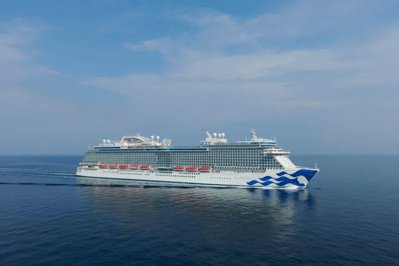 Majestic Princess Cruises ship with blue wave logo sails on calm ocean under partly cloudy sky