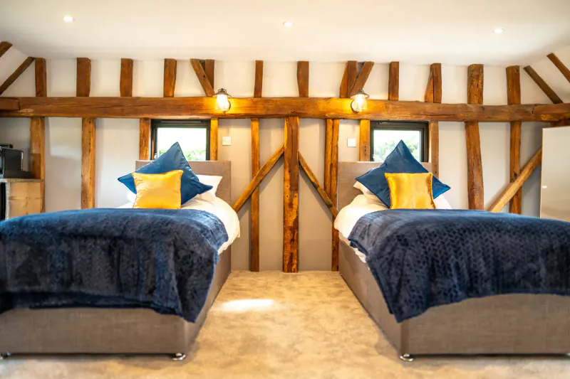 Luxurious twin bedroom in Chart Hills' The Barn with navy beds, yellow pillows, exposed wooden beams.