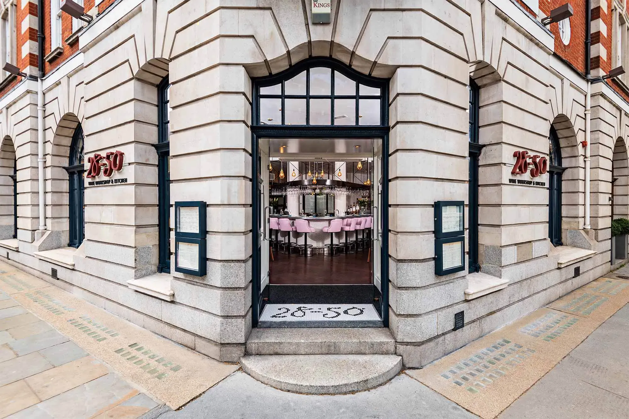 28-50 restaurant entrance on corner building with ornate white stone facade, open doors revealing pink tables inside, red '28-50' signage.
