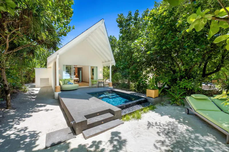 White thatched-roof villa with private plunge pool, green loungers, and tropical foliage in Maldives resort