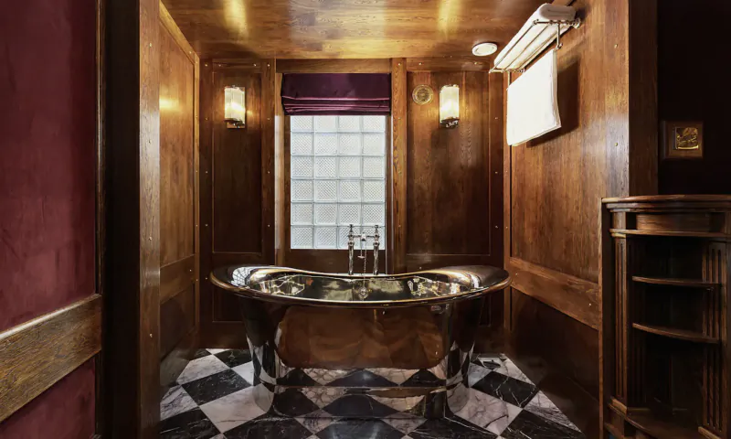 Luxurious wooden bathroom with clawfoot bathtub, purple curtains, checkered floor at House of Gods Hotel, Edinburgh