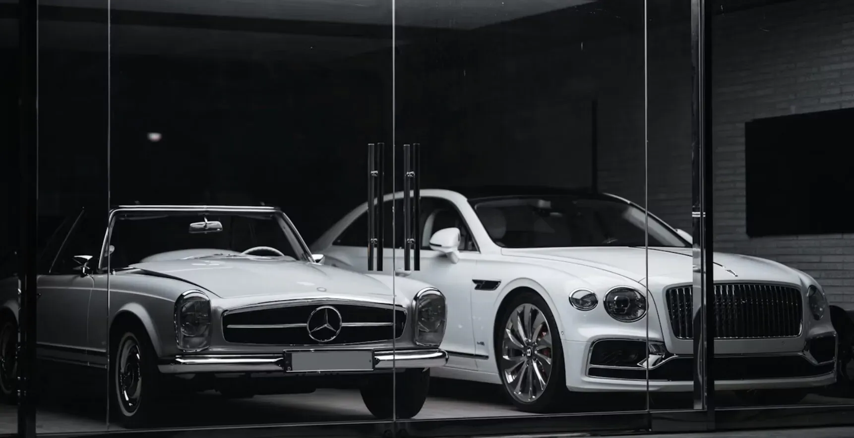 White classic Mercedes-Benz SL and Bentley coupe parked side-by-side in modern glass garage