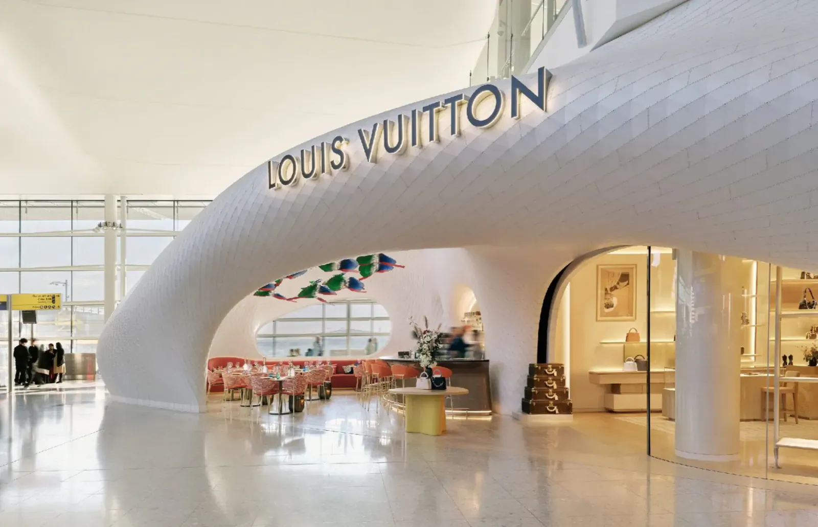 Louis Vuitton store and Le Café Cyril at Heathrow Airport, featuring white curved architecture, red chairs, and colorful decor.