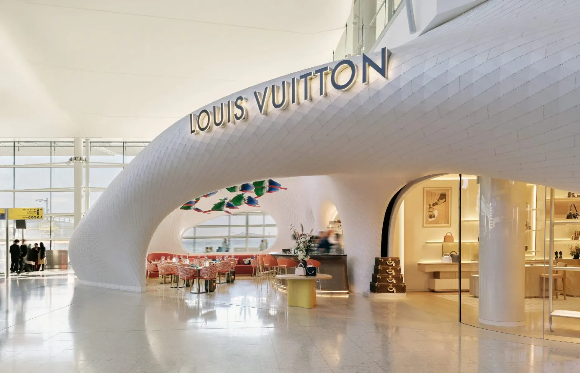 Louis Vuitton store and Le Café Cyril at Heathrow Airport, featuring white curved architecture, red chairs, and colorful decor.