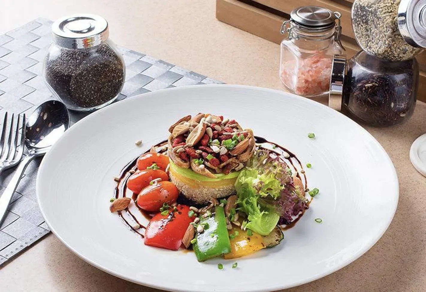 Stacked avocado tower with mushrooms, bacon, tomatoes, peppers, greens on white plate, surrounded by salt and pepper shakers