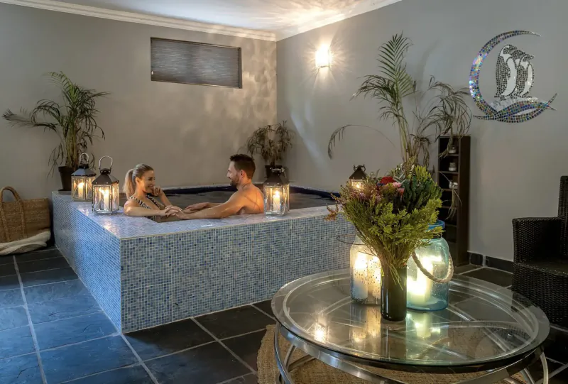 Romantic couple relaxing in candlelit hot tub at Tintswalo Boulders Boutique Hotel, surrounded by plants and lanterns