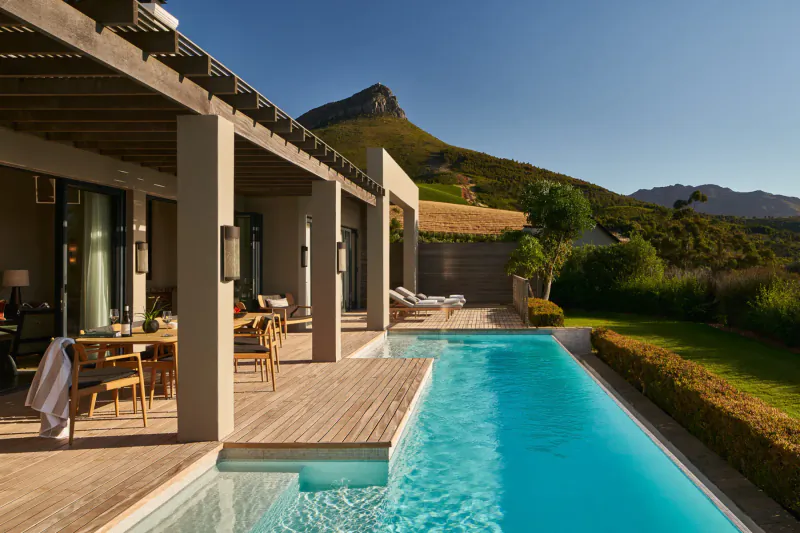 Luxury estate terrace with dining table, lounge chairs, infinity pool, and Cape Winelands mountains at Delaire Graff.
