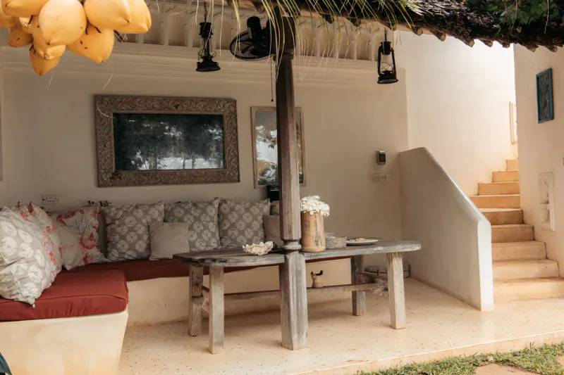 Serene Swahili outdoor lounge at Kijani Hotel Lamu: red cushions on white sofa, rustic table with flowers, lanterns, tropical setting.