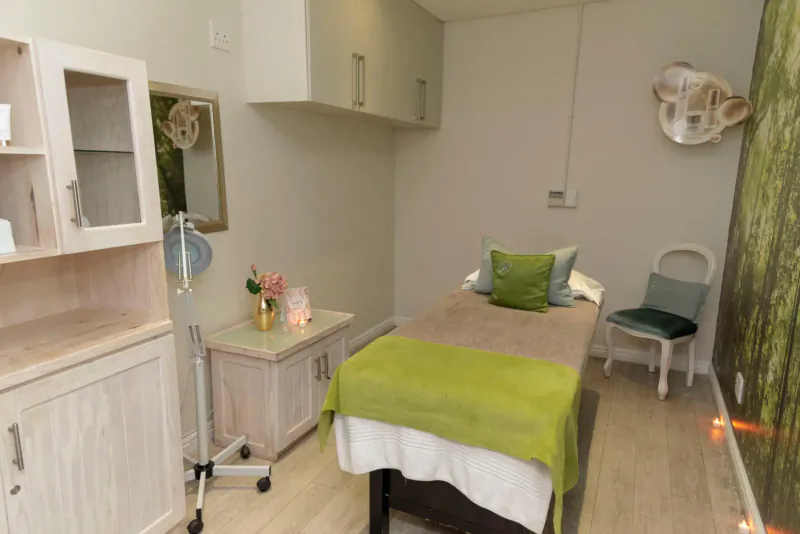 Cozy spa treatment room with green massage bed, koala wall art, plants, and green pillows on wooden floor