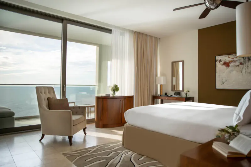 Elegant Jumeirah Port Soller Hotel suite with king bed, armchair, balcony overlooking sea.