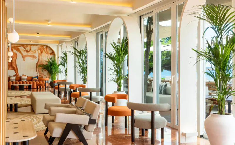 Elegant Hotel Riomar lounge in Ibiza with arched windows, orange chairs, palms, and orange mural