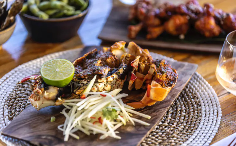 Grilled crab with lime wedge, papaya slaw, edamame, and chicken wings on wooden board at Rokuni Antigua