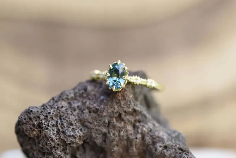 Close-up of gold ring with oval green gemstone and diamond accents on rough rock