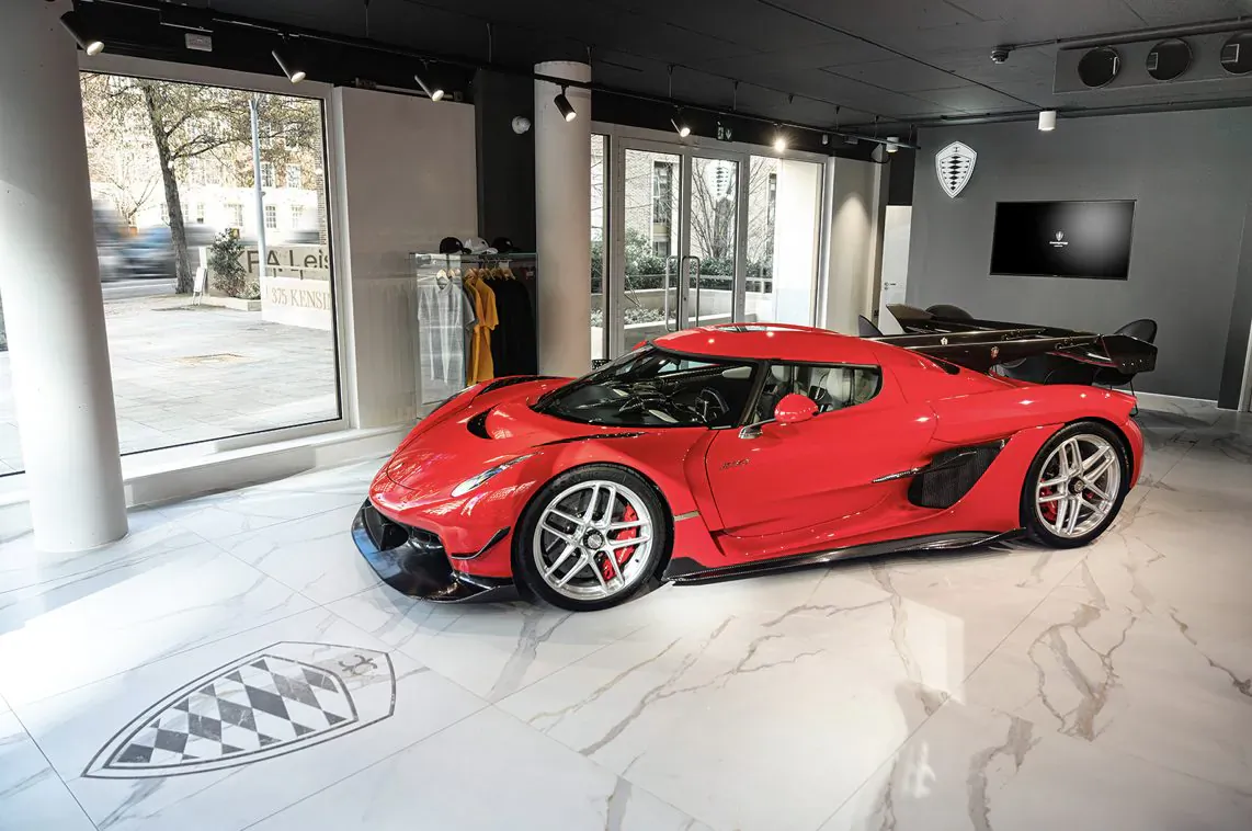 Red Koenigsegg hypercar with wing on showroom floor at UK dealership in London, checkered logo on marble