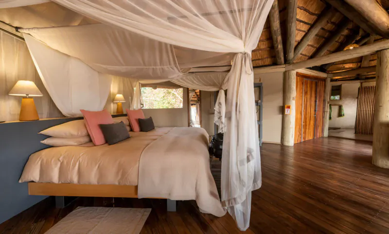 Luxurious bedroom in Lion Camp with mosquito net canopy over beige bed, pink pillows, lamps, and wooden interior