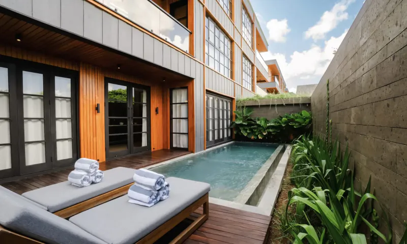 Luxury Bali villa poolside deck with lounge chairs, towels, wooden accents, and tropical plants against modern walls.