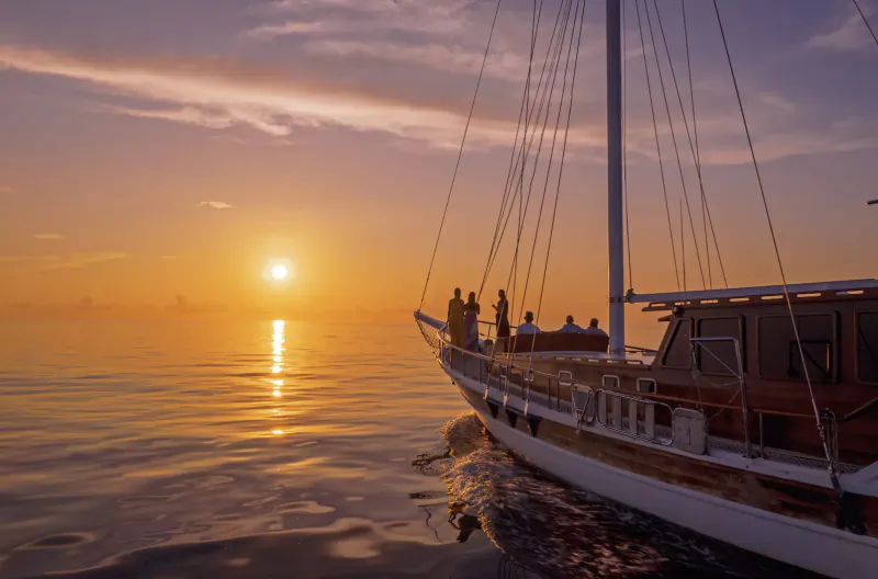 Silhouetted people on a gulet sailboat at sunset over the Indian Ocean at Mirihi Island Resort