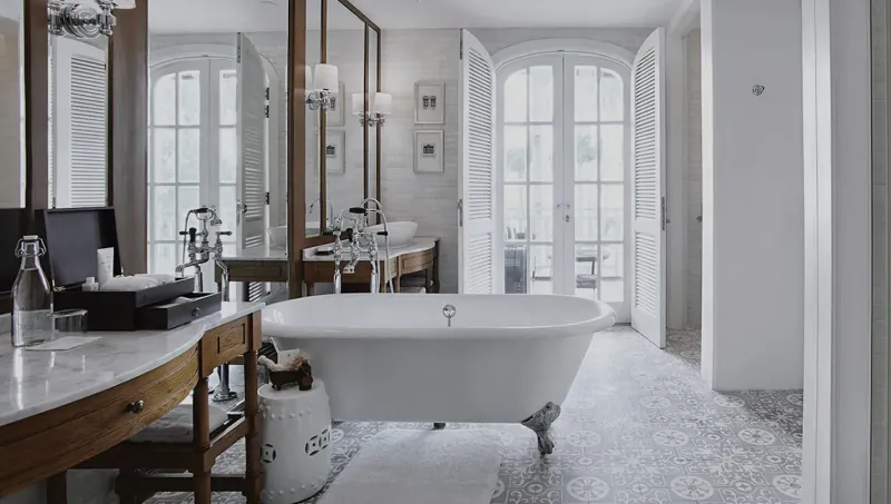 Elegant luxury bathroom at The Sanchaya with clawfoot bathtub, double vanity, mirrors, and French doors to balcony.