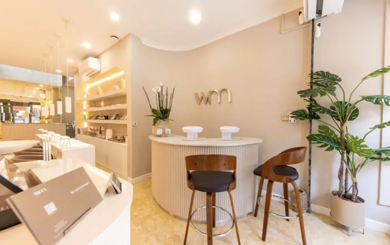 Modern WON nail spa reception with curved white counter, wooden stools, plants, and products in chic setting