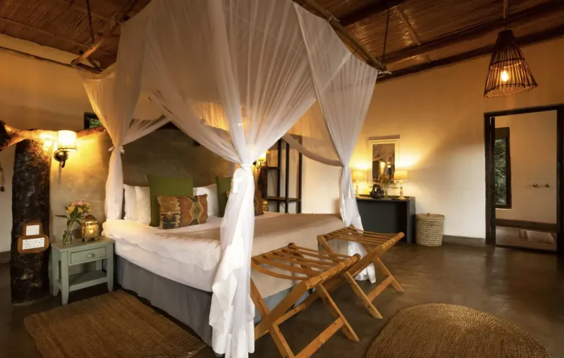 Eco-luxury bedroom in Maasai Mara with canopy bed, wooden accents, lanterns, and warm lighting.