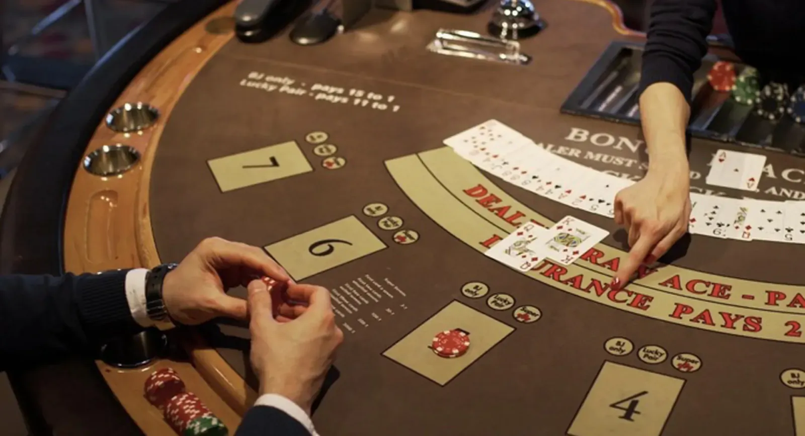 Close-up of blackjack table: dealer and player hands dealing cards, chips, 'BONUS', 'INSURANCE PAYS 3 to 2' text.