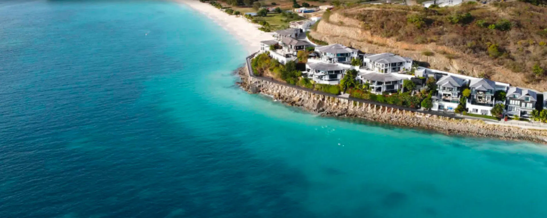 Aerial view of Tamarind Hills luxury villas perched on a cliff above turquoise Caribbean beach in Antigua.